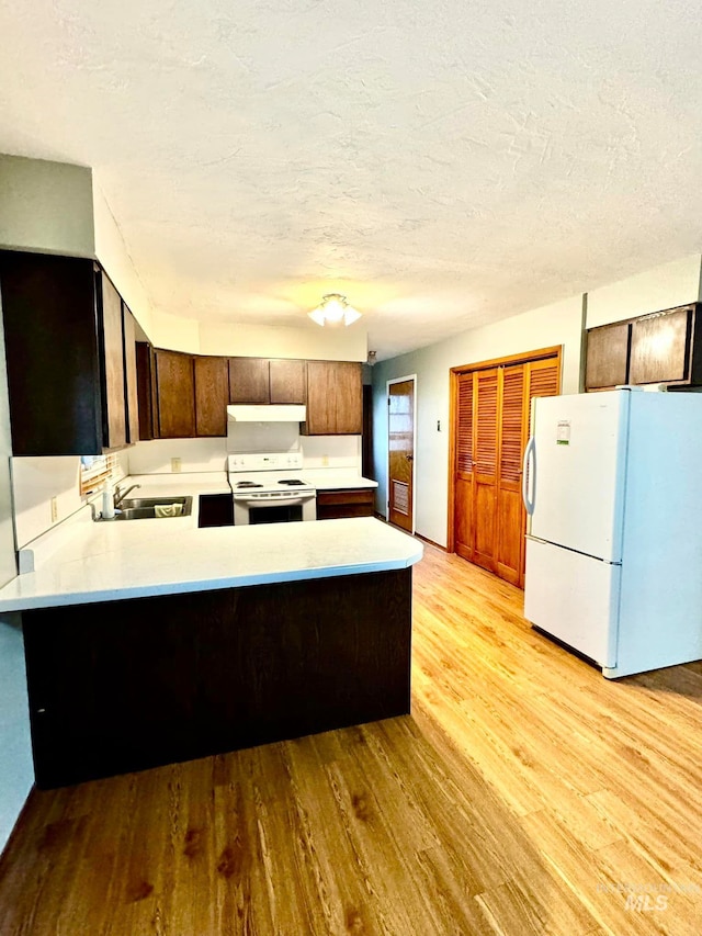 kitchen with kitchen peninsula, a textured ceiling, light hardwood / wood-style flooring, sink, and white appliances