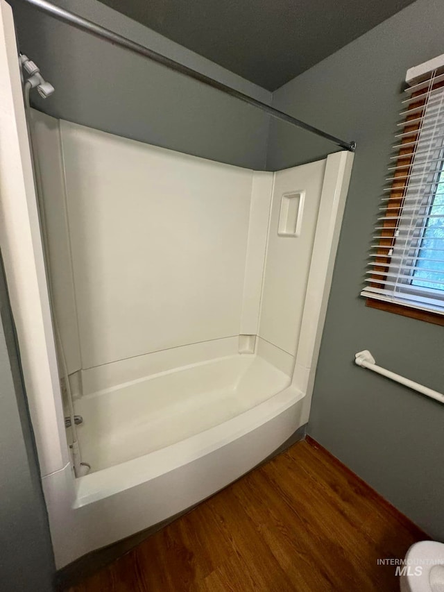 bathroom with washtub / shower combination, wood-type flooring, and toilet