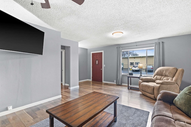 living area with ceiling fan, a textured ceiling, baseboards, and wood finished floors