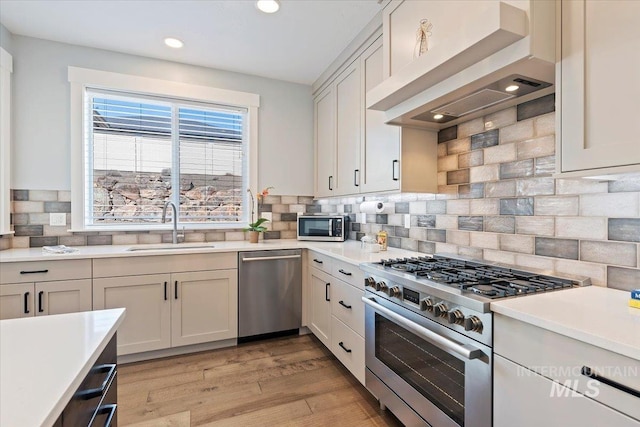 kitchen with wall chimney range hood, appliances with stainless steel finishes, light countertops, and a sink