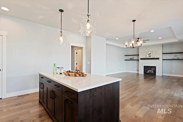 kitchen featuring a large fireplace, wood finished floors, light countertops, dark brown cabinets, and a tray ceiling