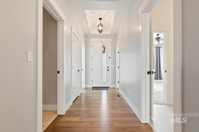 entrance foyer featuring a raised ceiling, visible vents, light wood-style flooring, an inviting chandelier, and baseboards