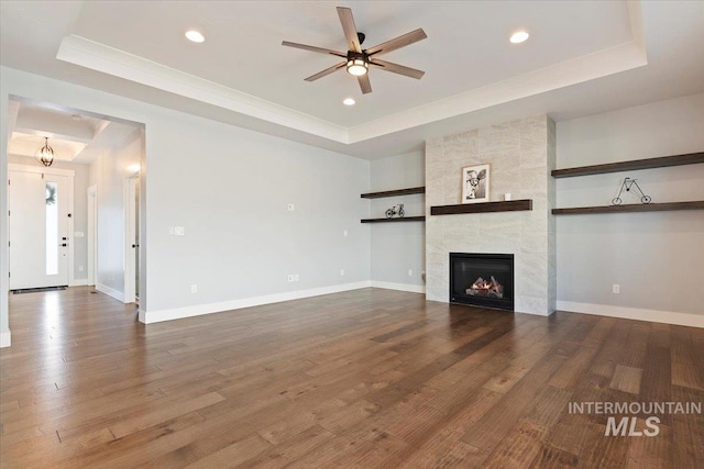 unfurnished living room featuring dark wood-style floors, a tray ceiling, and baseboards