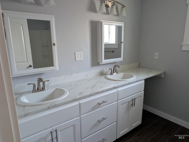 bathroom featuring double vanity, wood finished floors, baseboards, and a sink