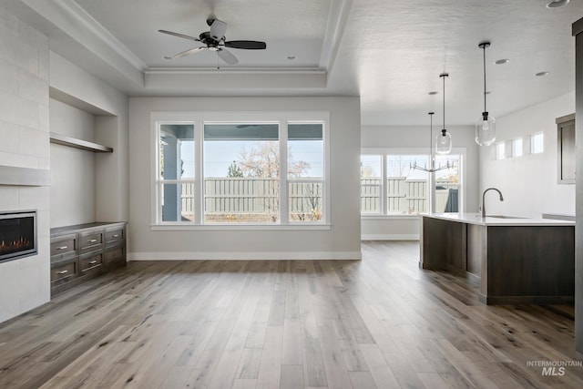 unfurnished living room featuring a raised ceiling, wood finished floors, a sink, a tiled fireplace, and ceiling fan