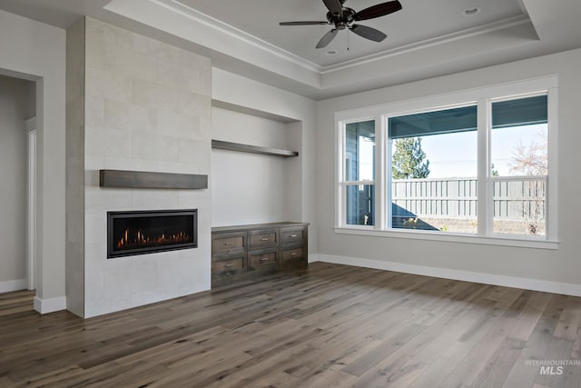 unfurnished living room with a tiled fireplace, wood finished floors, a raised ceiling, and a ceiling fan