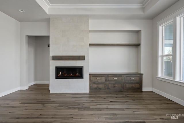 unfurnished living room with a tray ceiling, dark wood finished floors, and a tile fireplace