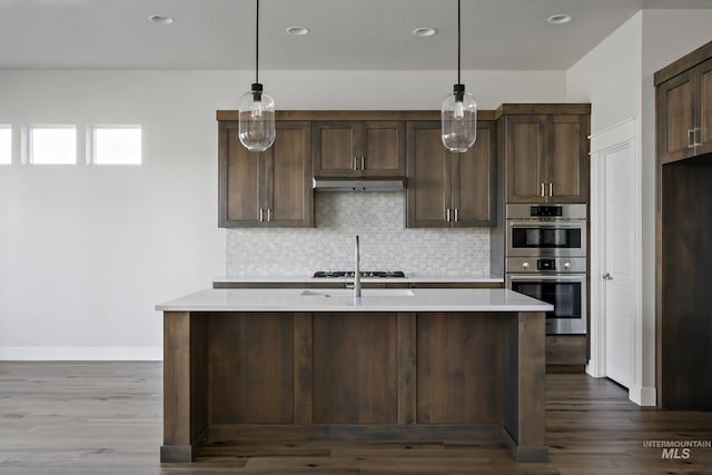 kitchen with double oven, under cabinet range hood, light countertops, dark brown cabinetry, and tasteful backsplash