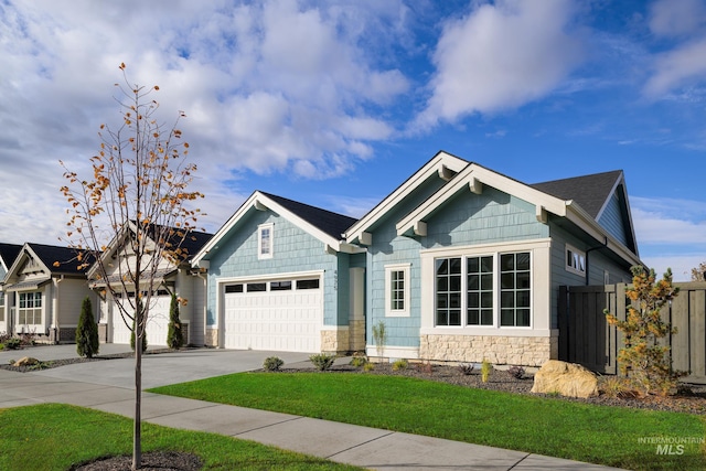 view of front of property with fence, a front lawn, concrete driveway, an attached garage, and stone siding