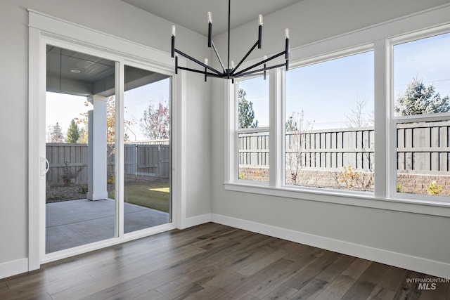 unfurnished dining area with a chandelier, baseboards, and dark wood-style floors