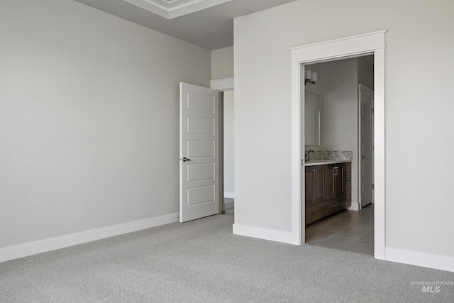 unfurnished bedroom with a sink, ensuite bathroom, light tile patterned flooring, light colored carpet, and baseboards