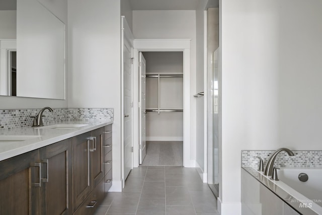 bathroom with a spacious closet, tile patterned floors, vanity, decorative backsplash, and tiled tub