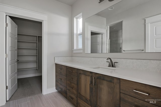 bathroom featuring a walk in closet, baseboards, and vanity