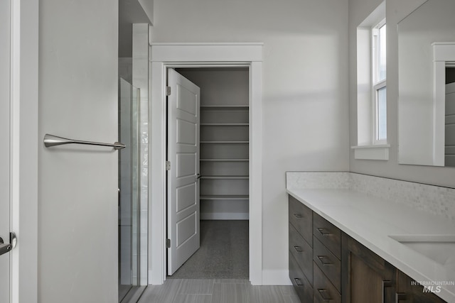 full bathroom featuring a walk in closet, baseboards, vanity, and a shower with shower door