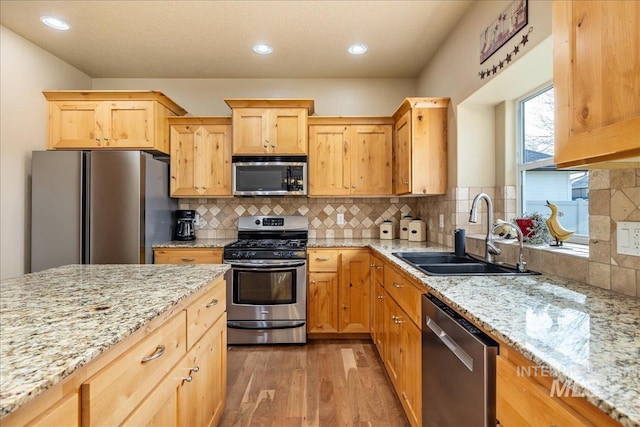 kitchen featuring light wood finished floors, light stone countertops, decorative backsplash, appliances with stainless steel finishes, and a sink