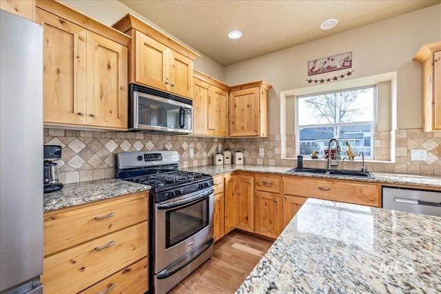 kitchen featuring light brown cabinetry, a sink, light stone counters, appliances with stainless steel finishes, and light wood finished floors