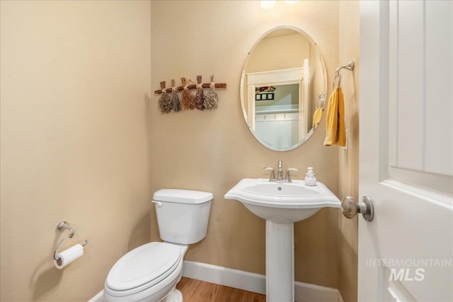 half bathroom featuring a sink, baseboards, toilet, and wood finished floors