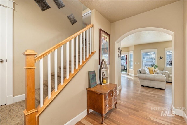 staircase featuring baseboards, arched walkways, a textured ceiling, and wood finished floors