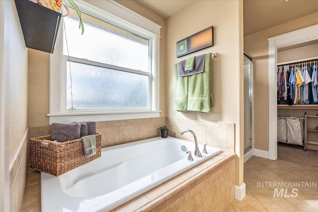 full bathroom featuring a walk in closet, a shower stall, a garden tub, and tile patterned floors