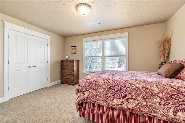 bedroom with a closet, light colored carpet, visible vents, and a textured ceiling