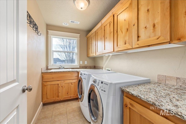 clothes washing area featuring visible vents, washing machine and clothes dryer, cabinet space, a sink, and a textured ceiling