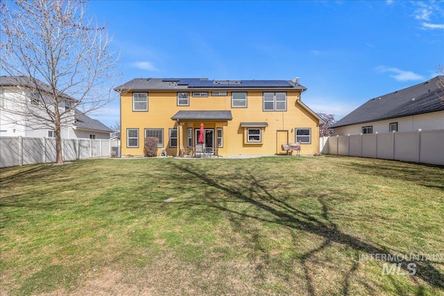 back of house with a yard, roof mounted solar panels, a patio, and a fenced backyard