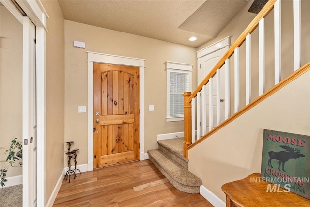 entrance foyer featuring a textured ceiling, wood finished floors, recessed lighting, baseboards, and stairs