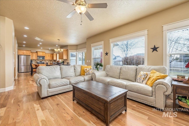 living area featuring plenty of natural light, light wood-style floors, ceiling fan with notable chandelier, and a textured ceiling