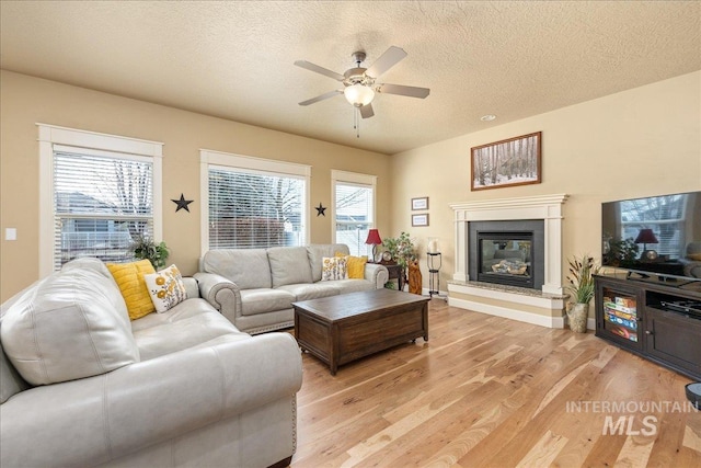 living area featuring a glass covered fireplace, plenty of natural light, a textured ceiling, and light wood-style flooring