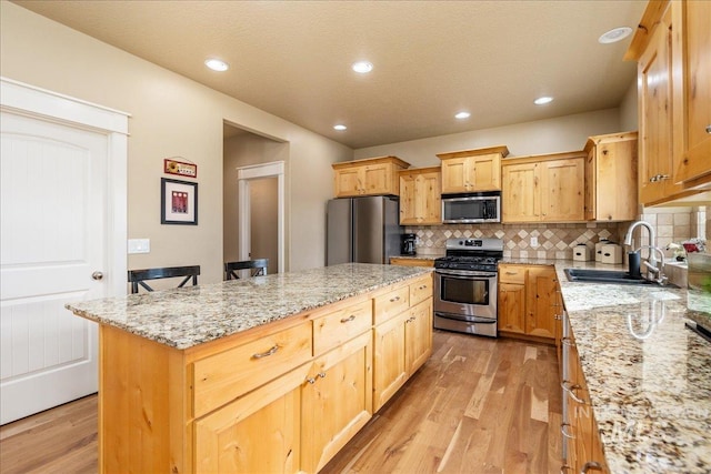 kitchen featuring light wood-type flooring, a sink, light stone counters, appliances with stainless steel finishes, and decorative backsplash