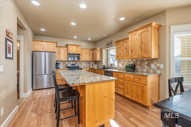 kitchen featuring stainless steel appliances, a kitchen island, light wood-style flooring, and decorative backsplash