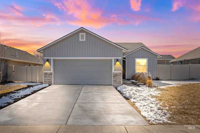 view of front of home with driveway, a garage, stone siding, fence, and board and batten siding