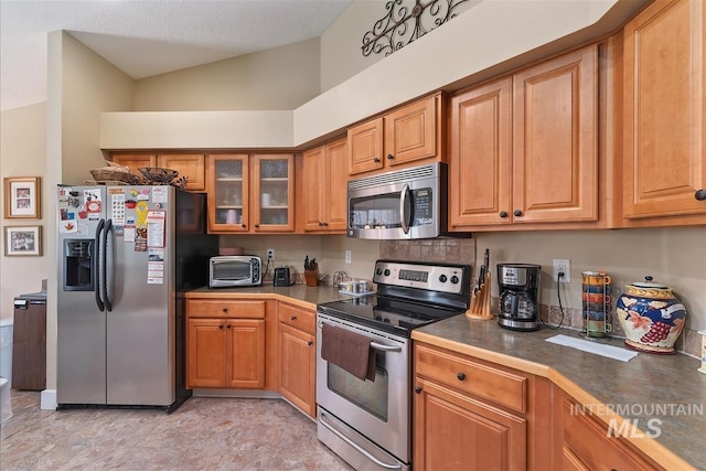 kitchen with brown cabinets, decorative backsplash, glass insert cabinets, a toaster, and appliances with stainless steel finishes