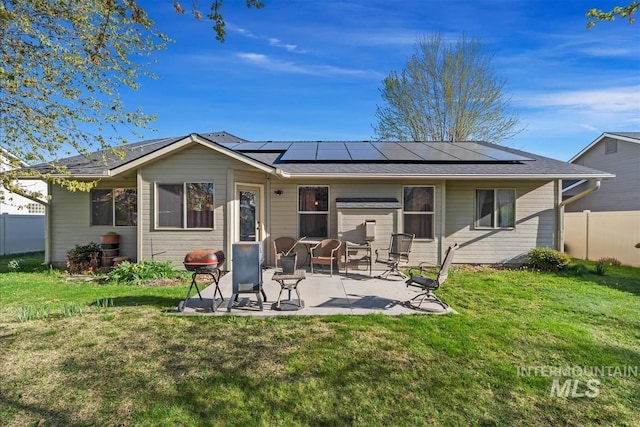rear view of property featuring fence, a patio, a lawn, and solar panels