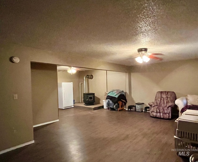 living area with a wood stove, dark wood-type flooring, a textured ceiling, and ceiling fan