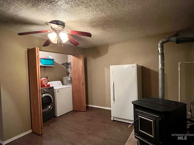 washroom featuring dark hardwood / wood-style floors, separate washer and dryer, a wood stove, ceiling fan, and a textured ceiling