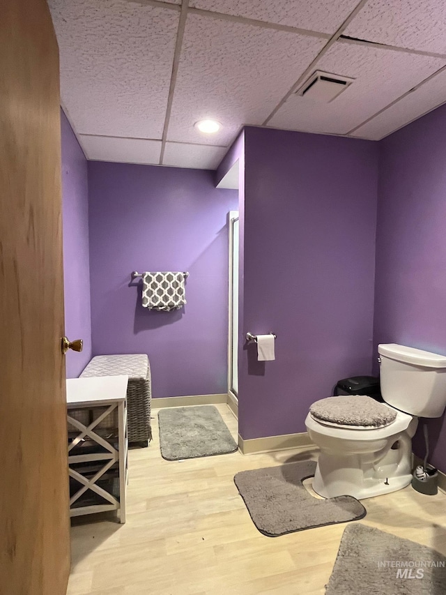 bathroom featuring hardwood / wood-style flooring, a shower with door, a paneled ceiling, and toilet