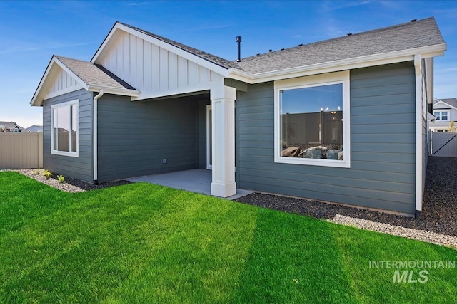 rear view of house featuring fence, a shingled roof, a lawn, a patio area, and board and batten siding