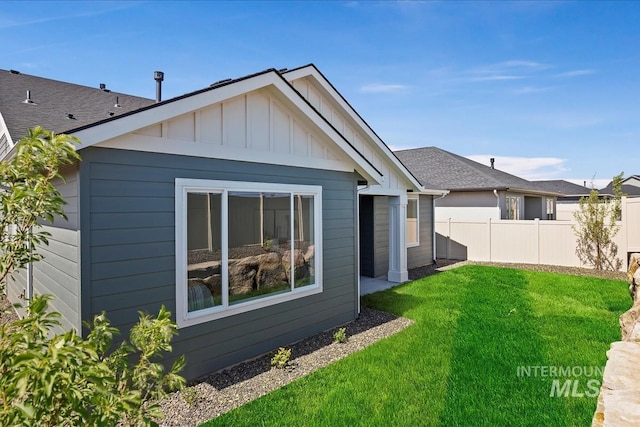 back of property with a lawn, board and batten siding, and fence