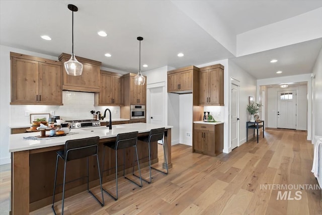 kitchen with backsplash, hanging light fixtures, oven, light hardwood / wood-style flooring, and a breakfast bar area