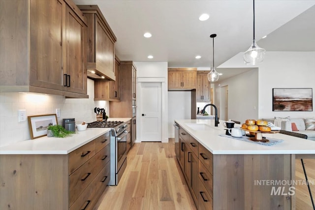 kitchen featuring light wood finished floors, backsplash, pendant lighting, appliances with stainless steel finishes, and a sink