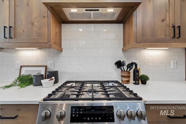 kitchen featuring stainless steel gas stove, brown cabinets, backsplash, range hood, and light countertops