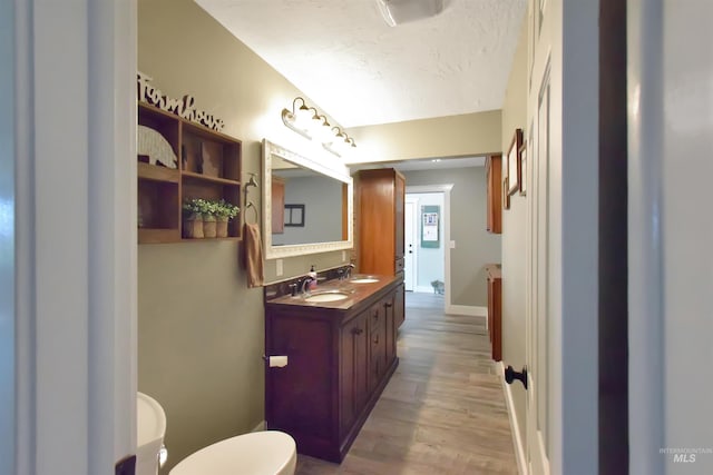 bathroom featuring wood-type flooring, toilet, vanity, and a textured ceiling
