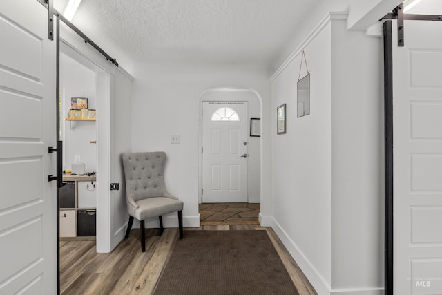 foyer with arched walkways, a barn door, a textured ceiling, and wood finished floors