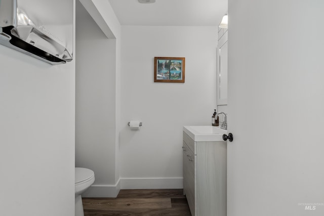 half bath with toilet, vanity, wood finished floors, and baseboards