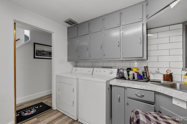 laundry area featuring light wood-type flooring, visible vents, baseboards, cabinet space, and washer and clothes dryer