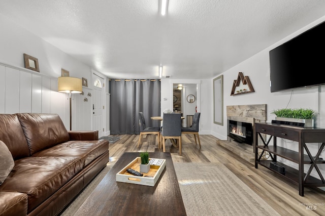 living area with a textured ceiling, wood finished floors, baseboards, and a glass covered fireplace