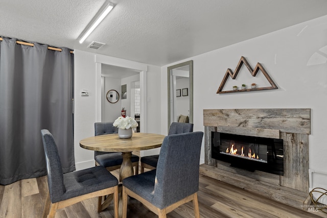 dining room featuring visible vents, a stone fireplace, wood finished floors, and a textured ceiling