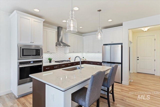 12740 S Alzano Way, Nampa, ID 83686 - kitchen with appliances with stainless steel finishes, wall chimney exhaust hood, a sink, decorative backsplash, and light wood-type flooring