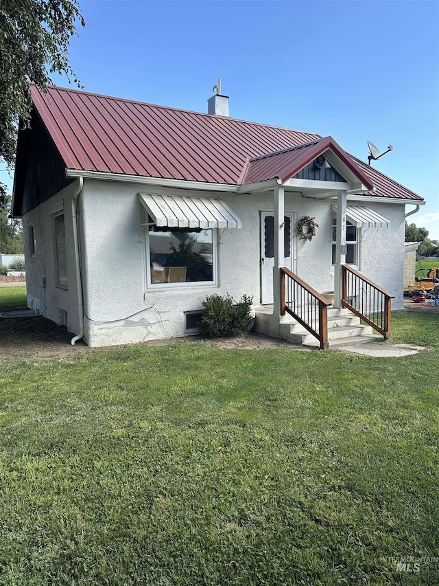 back of property with a yard, a chimney, stucco siding, a standing seam roof, and metal roof